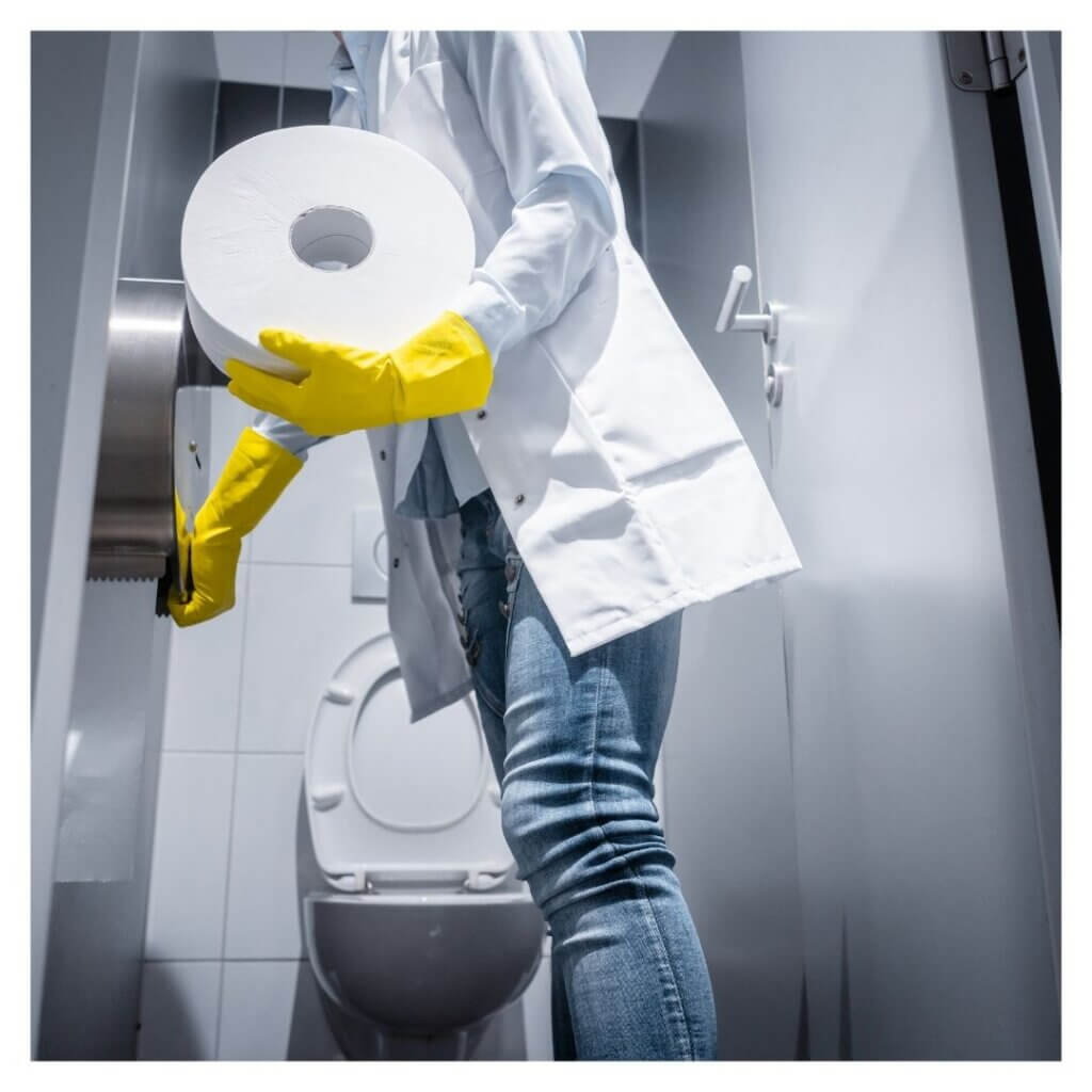 person stocks a large roll of toilet paper in bathroom stall 