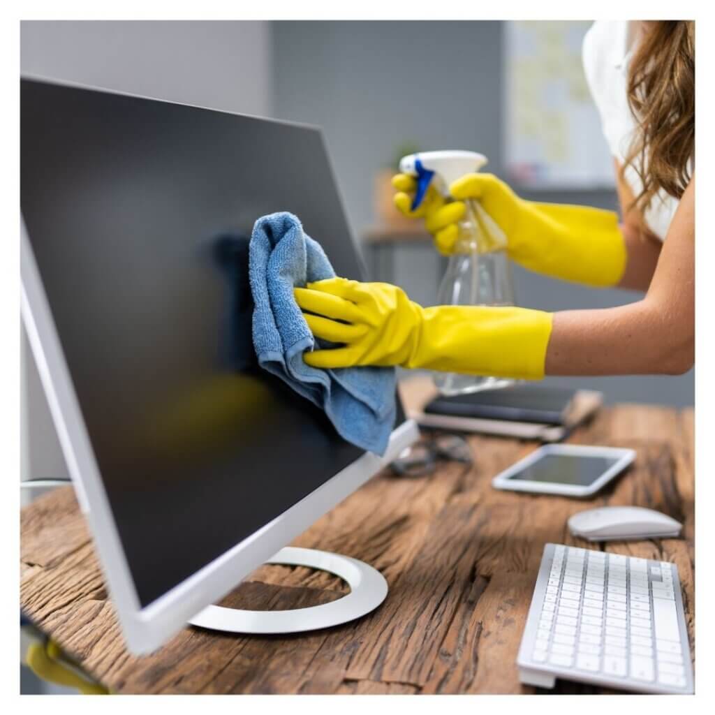 person wearing gloves wipes down computer monitor on desk 