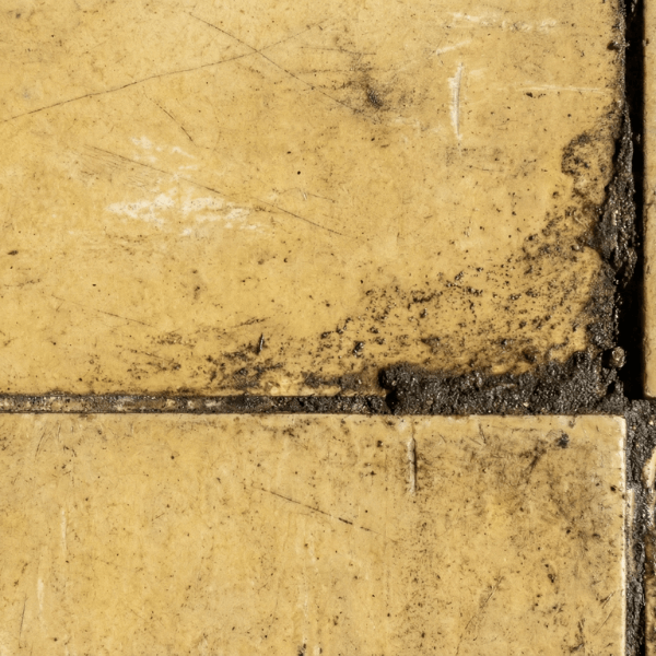 yellowed vinyl floor tiles showing dirt buildup in the corners and grout lines