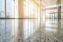 A brightly lit, modern commercial lobby featuring a highly polished terrazzo floor reflective surface.