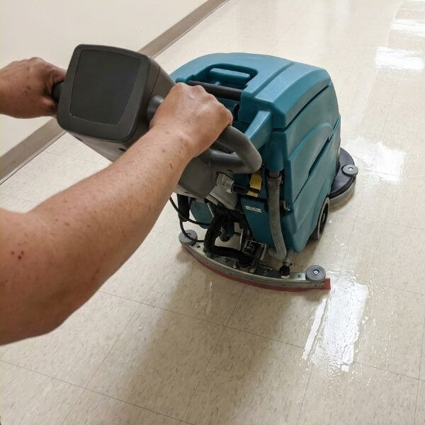 A commercial floor scrubber machine in operation on a VCT hallway floor, showing a clean trail behind it.