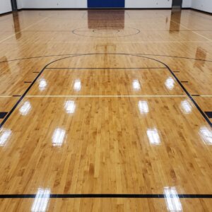 A brightly lit, recently waxed hardwood gymnasium floor showing clear painted game lines.