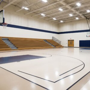 An interior view of an empty school gymnasium with folded bleachers and a clean hardwood floor.
