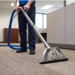 A service technician operates a commercial carpet cleaning machine in a modern office.
