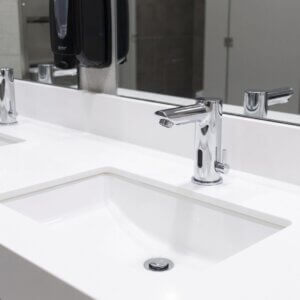 A detailed focus on a gleaming, clean modern office restroom sink and automatic faucet.